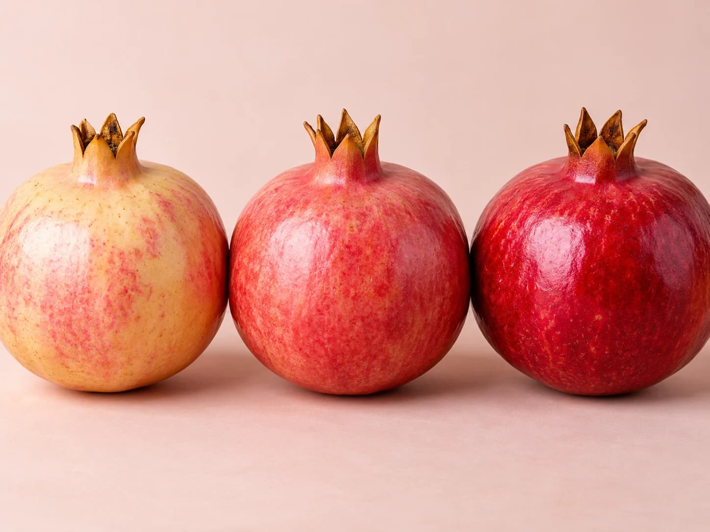 Three intact pomegranates with pale pink, pink-red, and deep red rinds